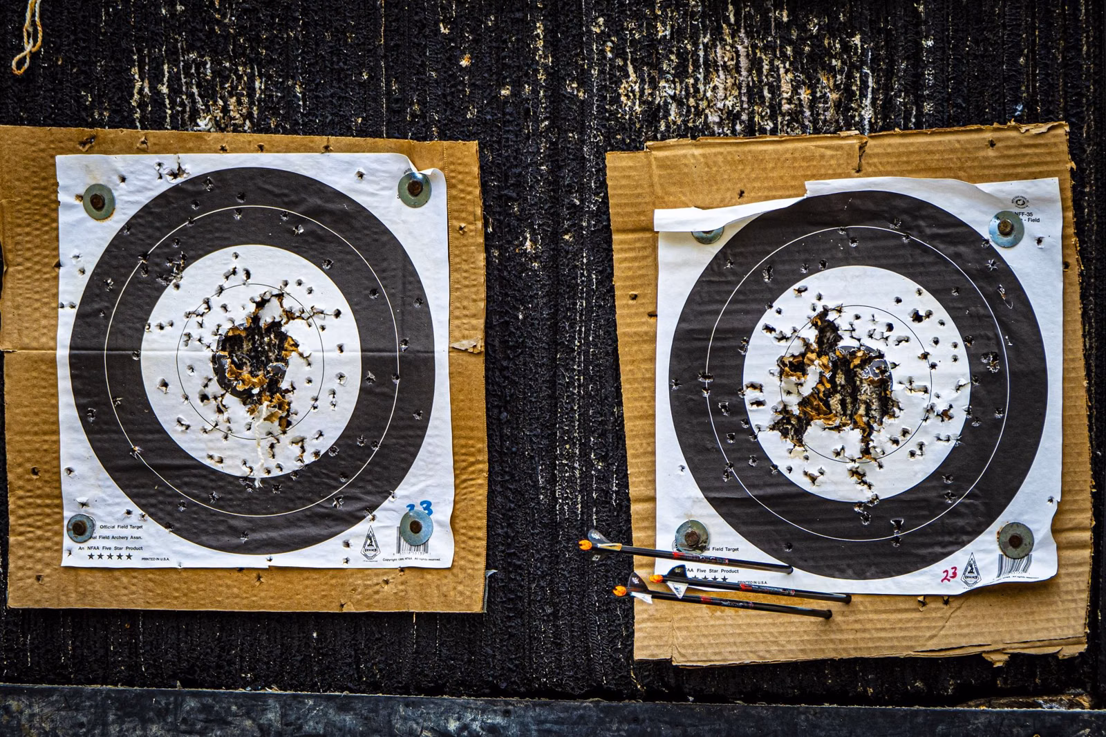 Two paper archery targets full of arrow holes at an outdoor range (not Bear Brook)